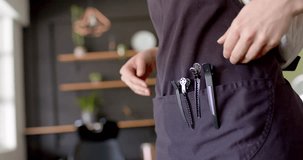 Midsection of caucasian female hairdresser in apron with hands and hair clips in pocket, slow motion. Local business, work, business owner, hairdressing, hair salon and hair