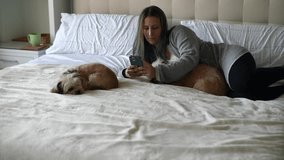 Woman lying in bed with dogs using cell phone
