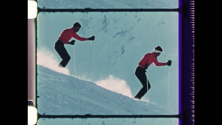 1982 Breckenridge, CO. Two Men carving down mountain sky slope. 1980s style fashion as men snow ski with golden sun ray behind heads. 4K Overscan of Vintage Archival film 