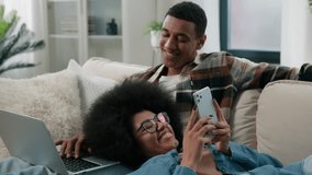 African American couple on couch man husband freelancer boyfriend working with laptop remote job with computer woman wife girlfriend scrolling mobile phone app social media at home sofa happy family - Powered by Shutterstock - Get 15% off with code: PIKWIZARD15