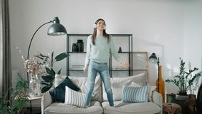 Video of funny woman listening to music with smartphone while dancing on the couch in the living room at home