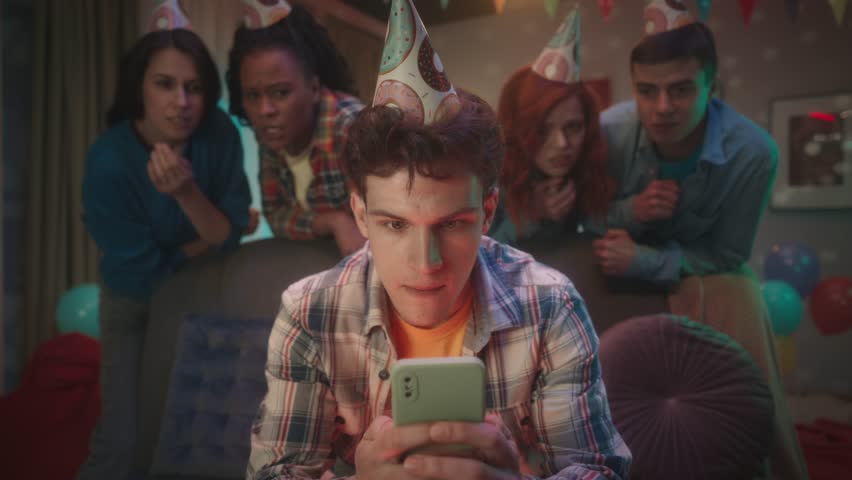 A guy is playing an online game on phone, his friends are watching him standing behind him. The guy loses, sighs sadly, waves his hand, his friends cheer him up, slap him on the shoulder. Slow motion. Royalty-Free Stock Footage #1104256709