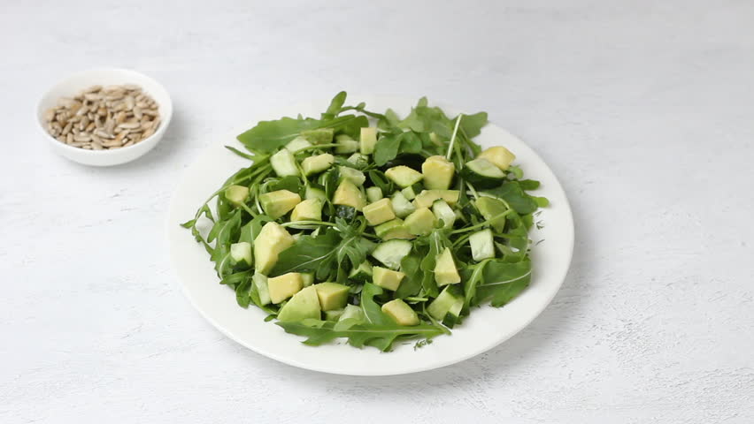 Salad of arugula, cucumbers and avocados are poured with yogurt dressing on a light gray background | Shutterstock HD Video #1104260101