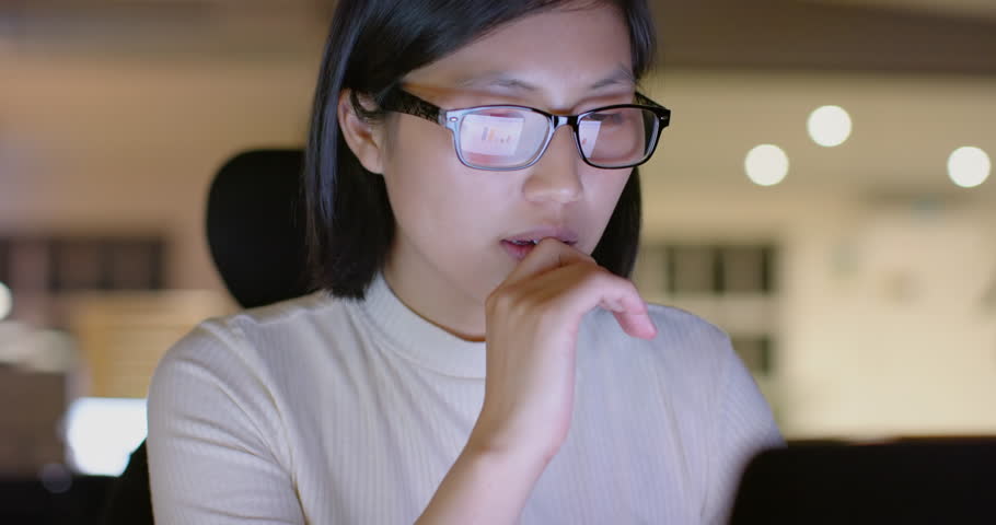 Focused asian casual businesswoman in glasses using laptop in office at night, slow motion. Business, communication, casual office, deadline and working late, unaltered.