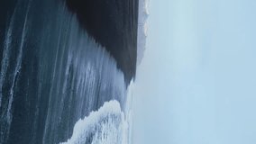 Vertical video: Aerial view of arctic black sand beach in iceland, beautiful ocean coastline with icelandic scenery. Spectacular atlantic shore with waves crashing on beaches, panoramic view. 60 fps