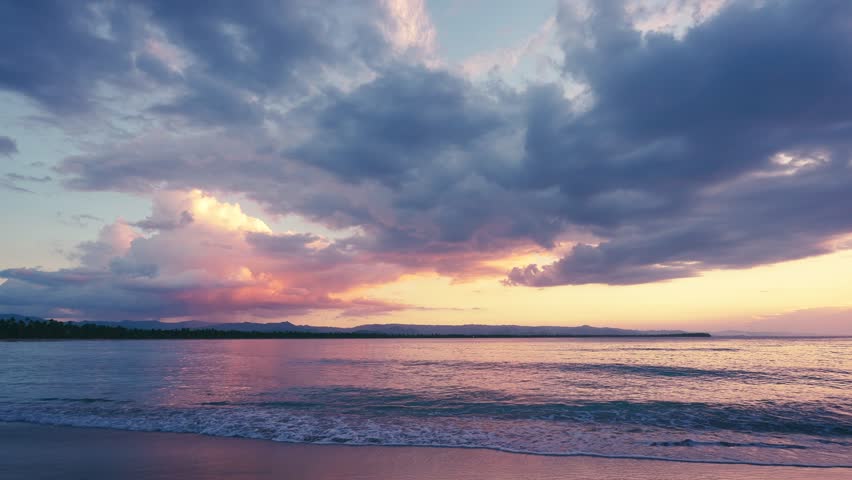 Scenic tropical sunset on the sandy beach. Waves on sand. Video of nature dawn landscape. Pink sky over the sea. Evening beach background. Orange clouds over the ocean. Best sunset in the world. 
