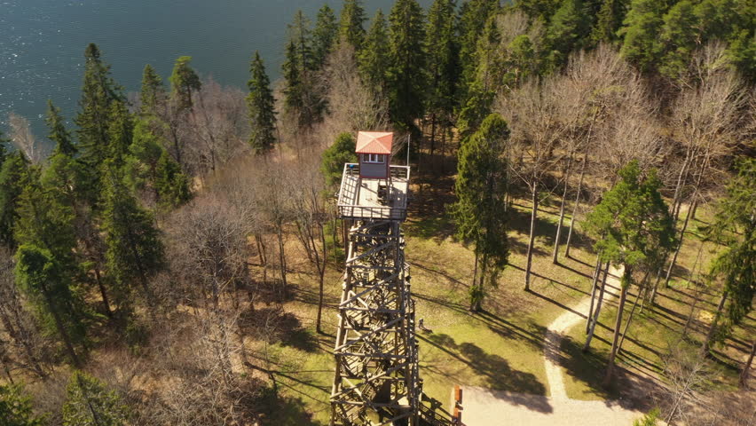 Wooden lookout tower on mountain hillside forest by lake sunny day, aerial orbit