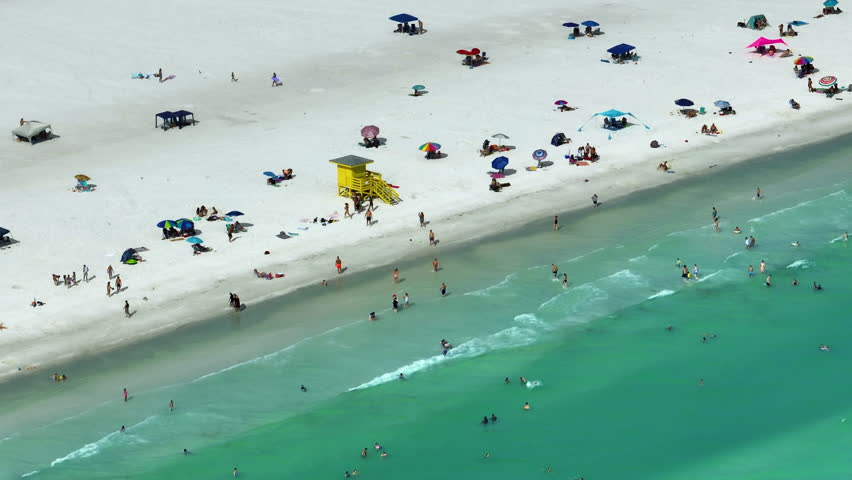 View from above of Siesta Key beach with white sands full of tourists in Sarasota, USA. Many people enjoing vacation time swimming in Mexica gulf water and relaxing on warm Florida sun