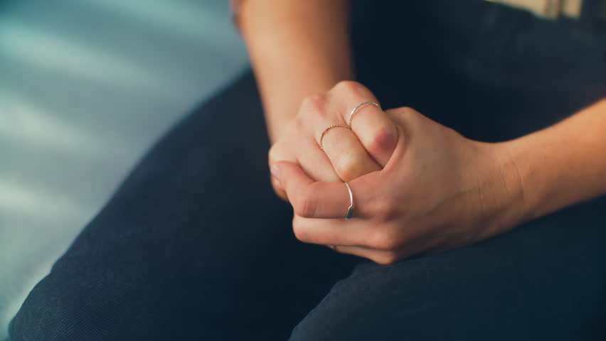 Nervous hands of a woman sitting on a blue therapy office sofa receives distressing news. Ideal for mental health awareness campaigns, counseling resources, and dramatic storytelling Royalty-Free Stock Footage #1104280031