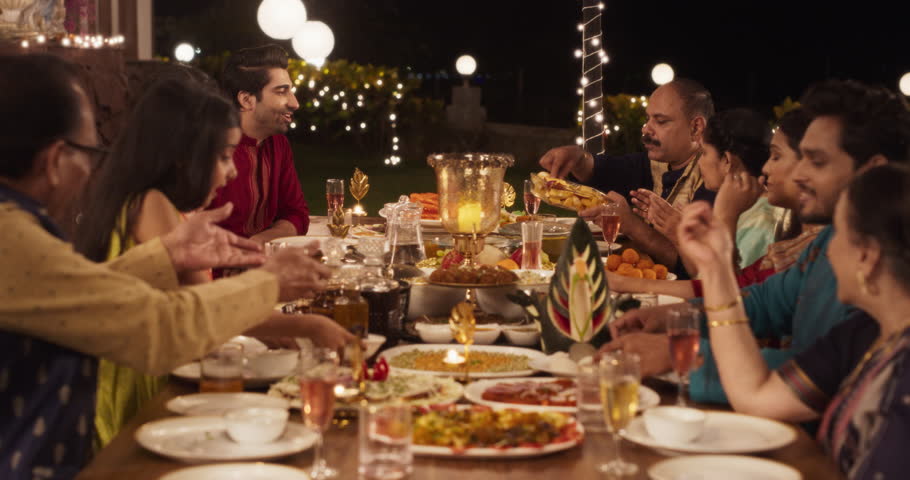 Happy Indian Family Having a Feast and Celebrating Diwali Together: Group of People of Different Ages in Their Traditional Clothes Eating Dinner Together in a Backyard Garden, Talking and Laughing Royalty-Free Stock Footage #1104284223