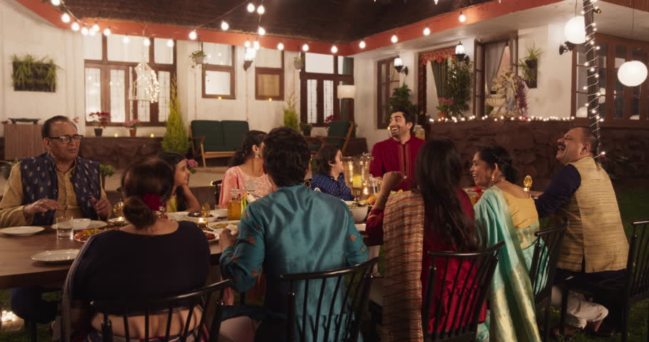Big Indian Family Celebrating Diwali: Family Gathered Together on a Dinner Table in a Backyard Garden Full of Lights. Group of People Sharing Food, Laughs and Stories on a Hindu Holiday. Slow Motion Royalty-Free Stock Footage #1104284249