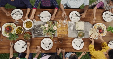 Big Indian Family Lunch Table: Top Down Elevated View at a Family and Friends Celebrating Outside at Home.Group of Children, Adults and Seniors Eating, Passing Traditional Dishes of Curry and Naan Video stock