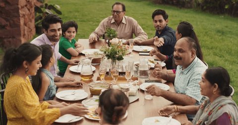 Indian Family Reunion: Young Adults, Seniors and Kids Gathered at a Table Outside a Beautiful Home. Friends and Family Have Fun, Eat and Drink. Garden Party Celebration in a Backyard. Static Shot Arkivvideo