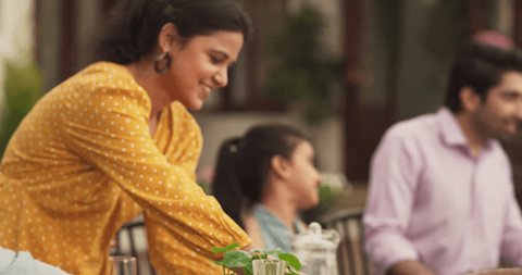 Indian Culture: Young Woman Hosting an Extended Family Gathering and Lunch at Home Backyard, Happily Serving Food to Her Guests of Family and Friends. Group of People Getting Together and Having Fun Video de stock
