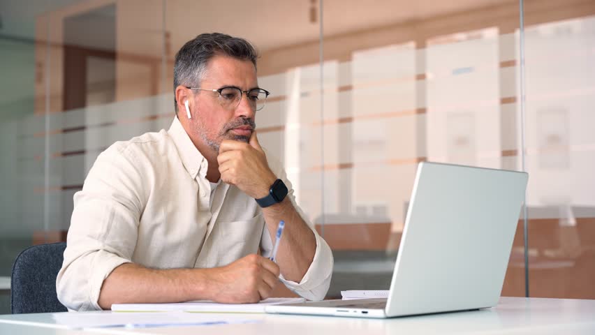 Middle-age Hispanic man using computer remote for business studying, watch online virtual webinar training meeting, video call. Smiling mature Indian or Latin businessman working on laptop in office. Royalty-Free Stock Footage #1104284995