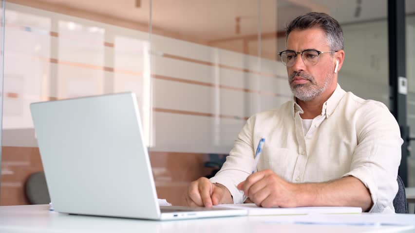 Middle-age Hispanic man using computer remote for business studying, watch online virtual webinar training meeting, video call. Smiling mature Indian or Latin businessman working on laptop in office. Royalty-Free Stock Footage #1104284997