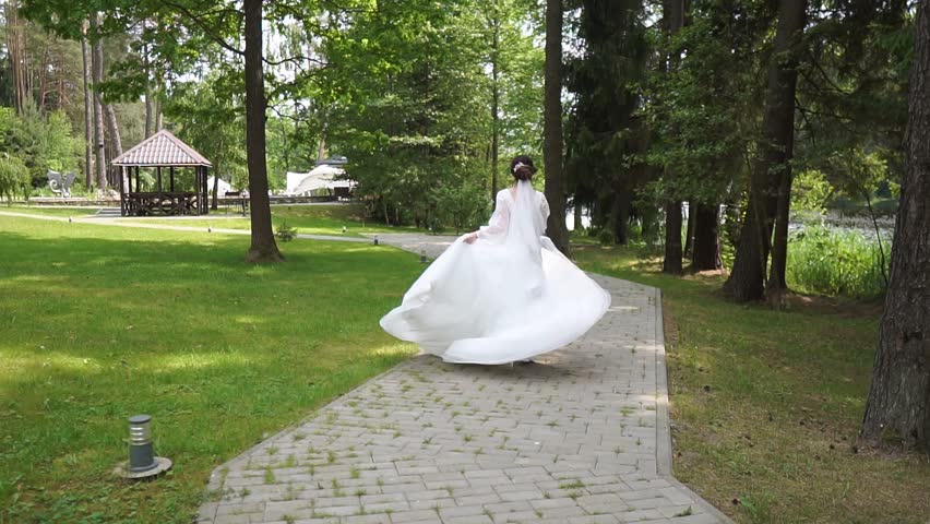 A beautiful bride in a luxurious white wedding dress runs along the path to meet the groom, rear view. Runaway Bride.  Royalty-Free Stock Footage #1104286693