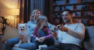 Joyful parents with daughter playing video games at home.