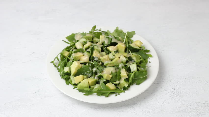 Salad of arugula, cucumbers and avocado with yogurt dressing sprinkled with sunflower seeds on a light gray background | Shutterstock HD Video #1104292985