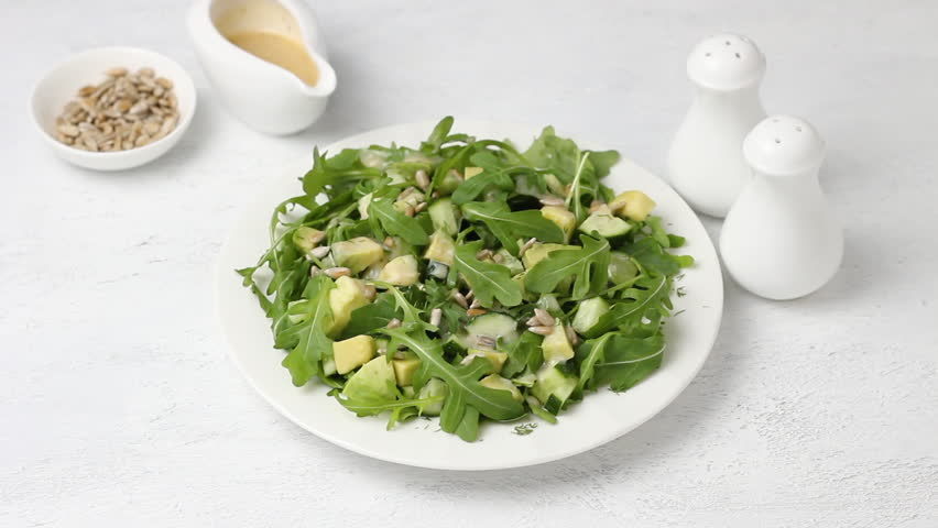 Salad of arugula, cucumbers, avocado with yogurt dressing and sunflower seeds on a light gray background | Shutterstock HD Video #1104295715