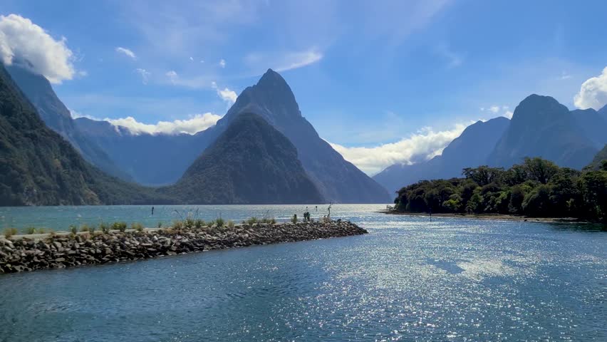 Mitre Peak (Rahotu in Māori language) in Milford Sound (Piopiotahi) with surrounding mountains. A sunny blue sky day in Fiordland National Park on the South Island of New Zealand. Royalty-Free Stock Footage #1104304883