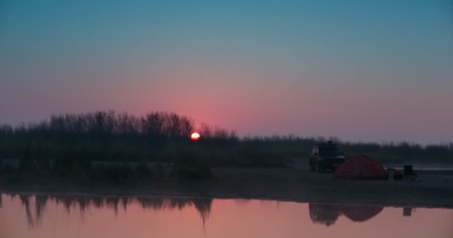 The SUV stands next to a stretched awning on the shore of the lake, surrounded by trees at sunset | Shutterstock HD Video #1104308641