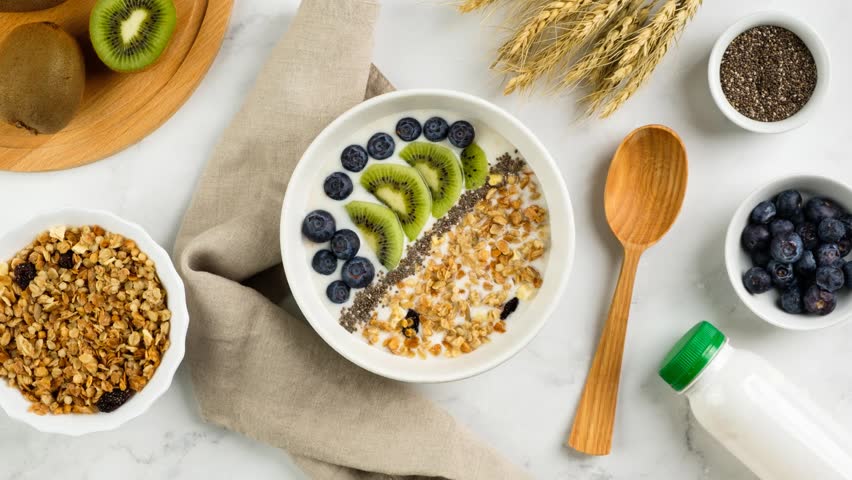 Zoom in healthy breakfast consisting of natural yogurt with granola, kiwi fruit, chia seeds and blueberries, top view. Concept of healthy food, vegetarian eating.  | Shutterstock HD Video #1104312667