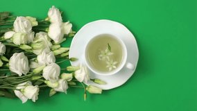 Healthy herbal tea in a white cup with Lisianthus flowers for relaxation and wellness. Floral Infusion, tea drinking ritual for a healthy lifestyle, white background,  top view, vertical video