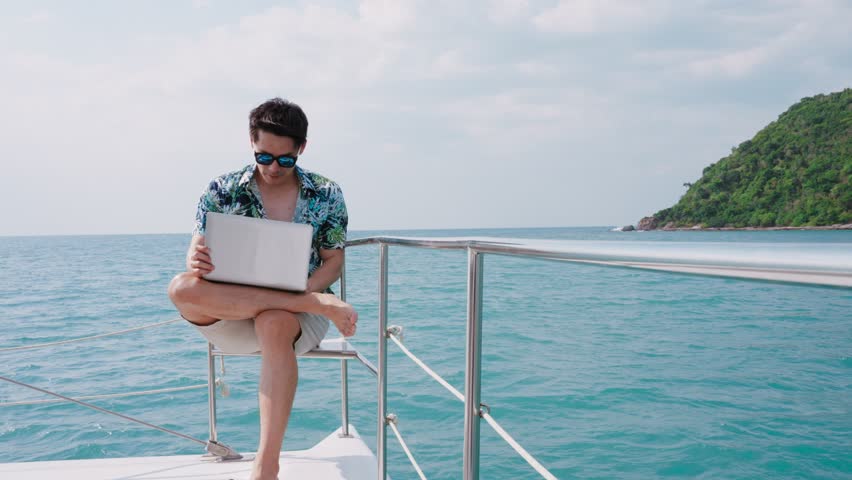Asian young businessman using laptop computer and working in sailboat. Freelance man working with notebook while vacation time in yacht, Travel and Vacation Concept. Royalty-Free Stock Footage #1104320877