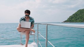 Asian young businessman using laptop computer and working in sailboat. Freelance man working with notebook while vacation time in yacht, Travel and Vacation Concept.