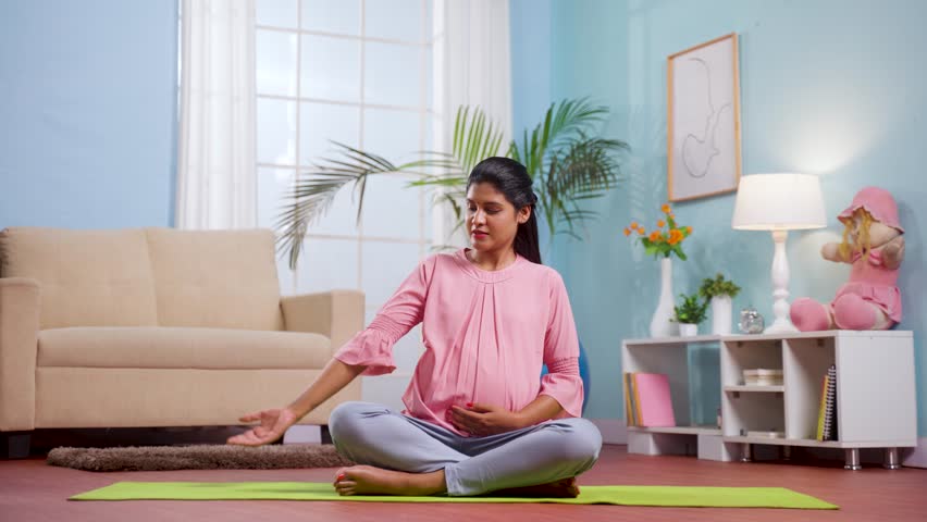 Indian pregnant woman at home doing yoga asana or exercise by sitting on yoga mat at home - concept of Prenatal fitness, Maternal well-being, Healthy pregnancy. Royalty-Free Stock Footage #1104322303