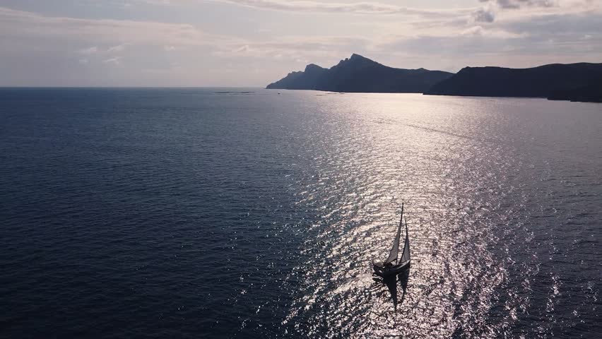 Sailboat sailing by coastline seashore against sunset and mountains. Sail boat in the south coast of Spain, Cartagena.