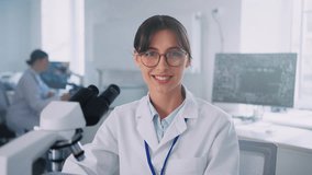 Close-up of young brunette woman wearing scientist uniform looking at camera. Attractive girl using modern microscope and experimenting in bright laboratory room. Daytime, working day. Job concept - Powered by Shutterstock - Get 15% off with code: PIKWIZARD15