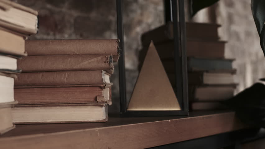 Old vintage books in craft paper cover lie on shelf near pyramid figure. 
