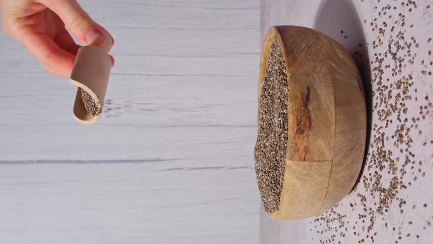 Slow motion chia seeds fall in wooden bowl. Vertical footage Healthy superfood rich in Omega 3 fatty acids. Dry healthy natural ingredient. Chia grains are falling | Shutterstock HD Video #1104333877