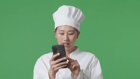 Close Up Of Asian Woman Chef Waving Hand Having A Video Call On Smartphone While Standing In The Green Screen Background Studio

