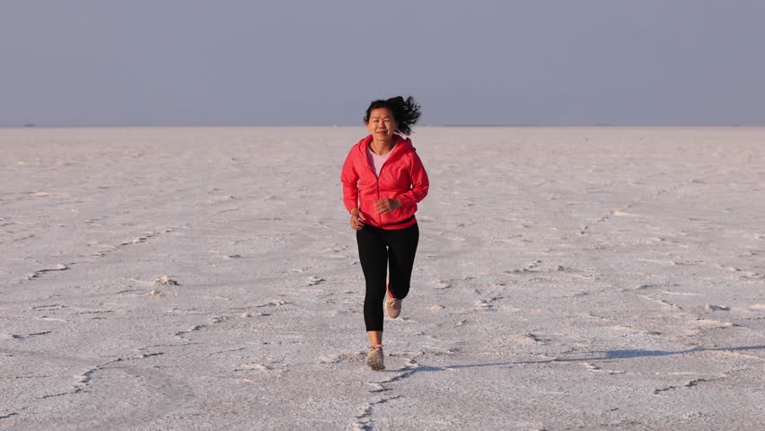 Asian woman jogging across the Bonneville Salt Flats flats in Utah. Slow Motion.