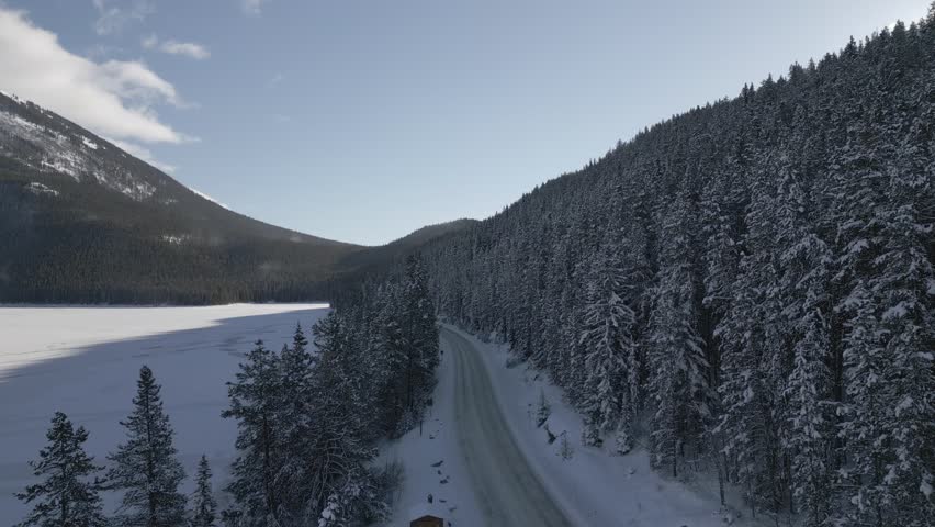 Aerial video flying over a car driving on the trails of Banff National Park in winter
