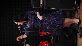 Happy charming woman musician singing song into microphone. Vertical video. Music band rehearsing at rehearsal studio, playing musical instruments and singing songs. Guitarist playing on guitar