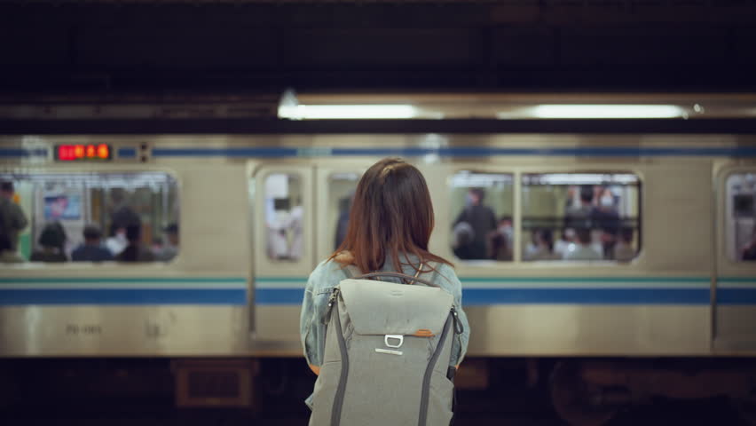Rear view of young woman with backpack while waiting at platform of subway train station looking at passing tram, slow motion, waiting for a trip. Royalty-Free Stock Footage #1104338493