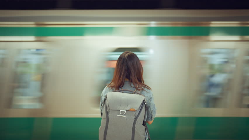 Rear view of young woman with backpack while waiting at platform of subway train station looking at passing tram, slow motion, waiting for a trip. Royalty-Free Stock Footage #1104338493
