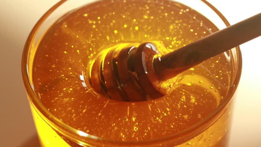 Honey in a transparent jar. A honey spoon is dipped in honey. Honey sparkles in the sun. Royalty-Free Stock Footage #1104338575
