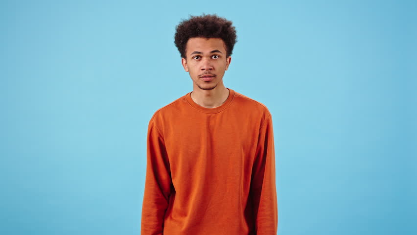 Excited fan watches game cheering actively. African American man covers face with hands and shakes head in disappointment after loss of favorite team in blue studio