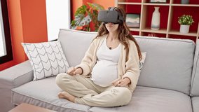Young pregnant woman playing video game using virtual reality glasses at home