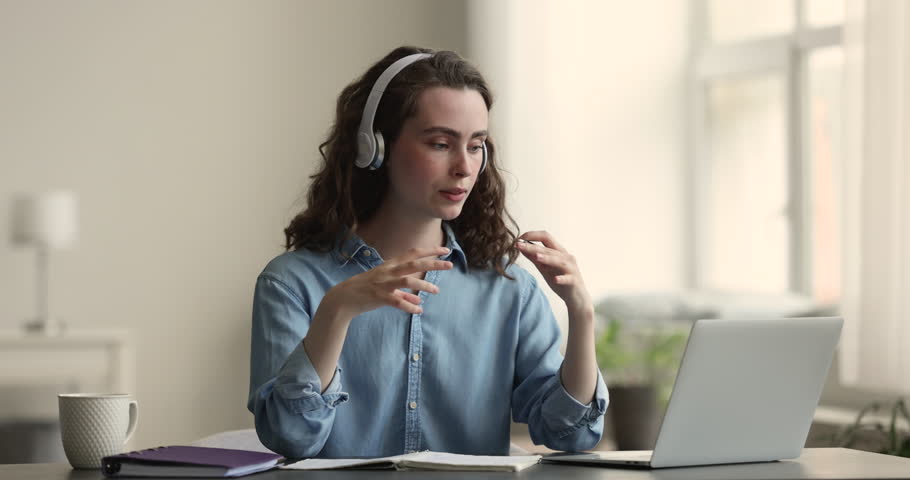Serious pretty young blogger woman in headphones giving workshop, speaking at laptop hand gestures, explaining webinar, talking on video call at home, broadcasting online Royalty-Free Stock Footage #1104348929
