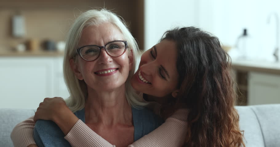 Loving grown up daughter cuddling and kissing on cheek her happy senior mum miss after long separation express love, enjoy tender moment sit on sofa during her visit, close up. Motherhood, family ties Royalty-Free Stock Footage #1104349039