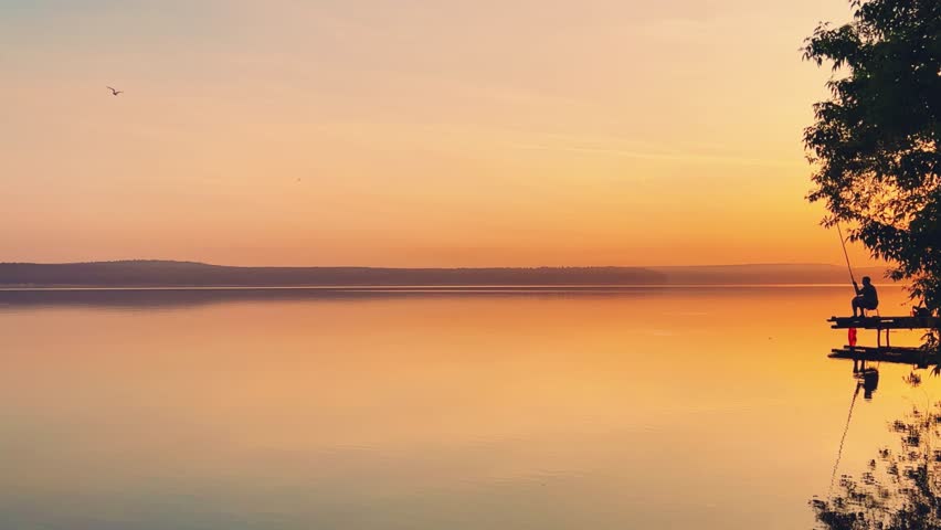 Side view of a fisherman on the pond. Fishing at sunset. Russian fisherman with fishing rods on the background of a pond and a golden sunset. Russia, Votkinsk