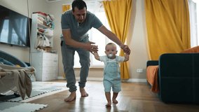 Baby first steps.Toddler at home takes funny first steps.Dad teaches child to walk, legs close-up.Toddler feet on laminate floor.Father's day child education.Kid dream study at home.walk baby learning - Powered by Shutterstock - Get 15% off with code: PIKWIZARD15