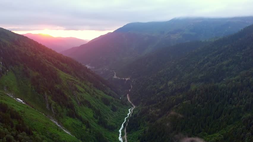 Aerial view of long deep valley with dark forest in mountains illuminated by red sun lights.