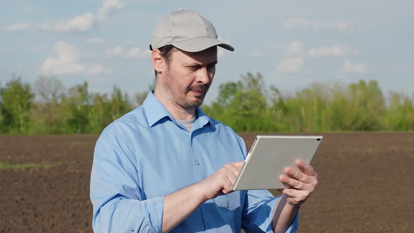 Businessman farmer works on plowed land of cultivated field in countryside on spring day. Agricultural industry. Farmer uses computer tablet, analyzes soil. Agricultural business concept. Farming Royalty-Free Stock Footage #1104359289